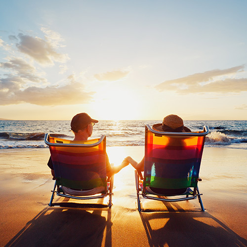 a couple sitting in beach chairs holding hands looking at the ocean during sunset